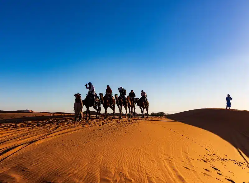 a group of people riding camels in the desert as one of our Morocco Activities