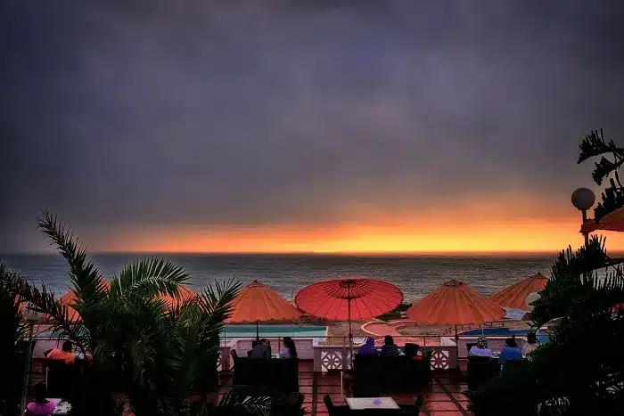 a group of people sitting on a deck with umbrellas overlooking the ocean